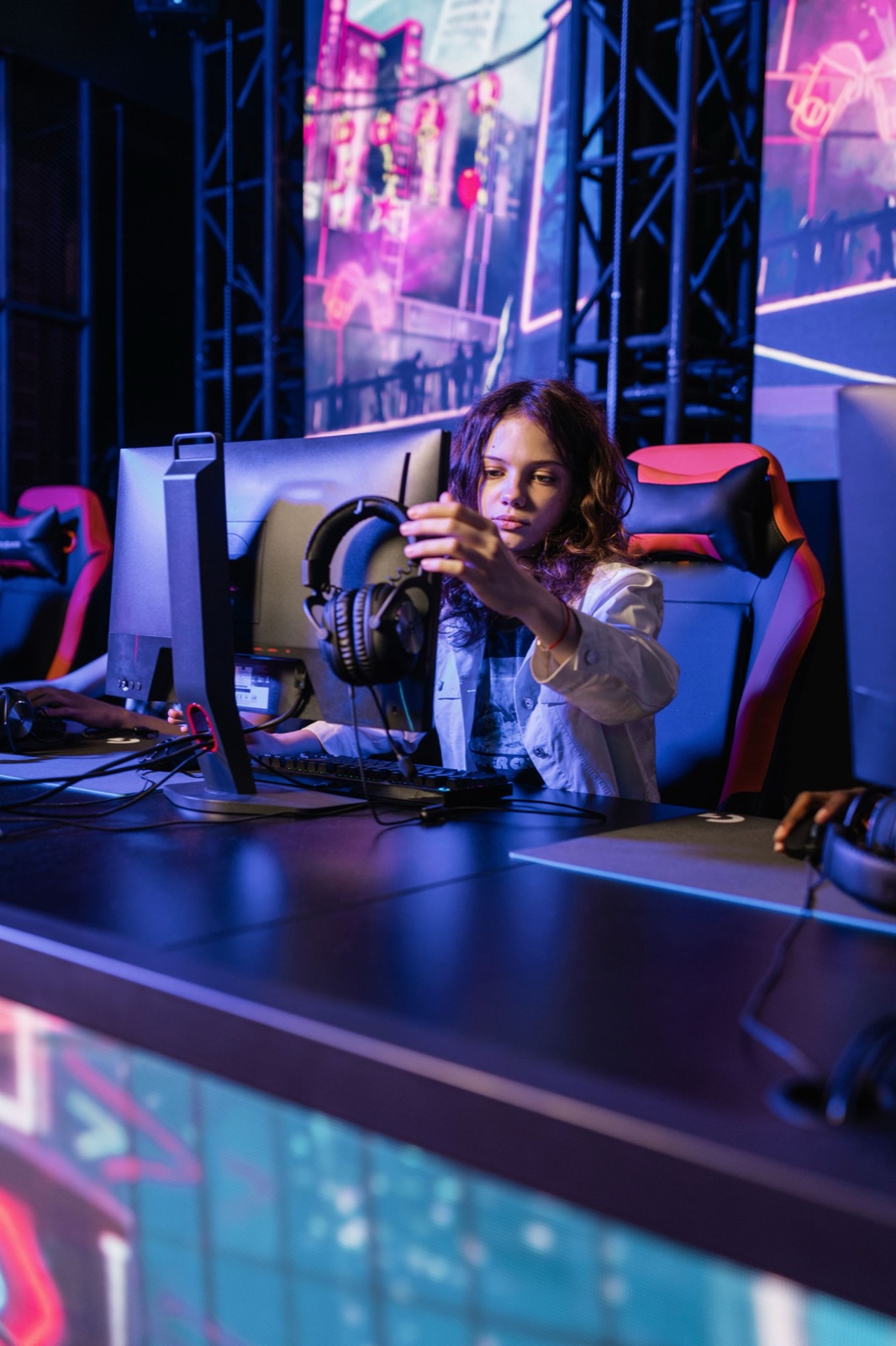 Giocatrice regola le cuffie a una postazione esports immersa in luci neon