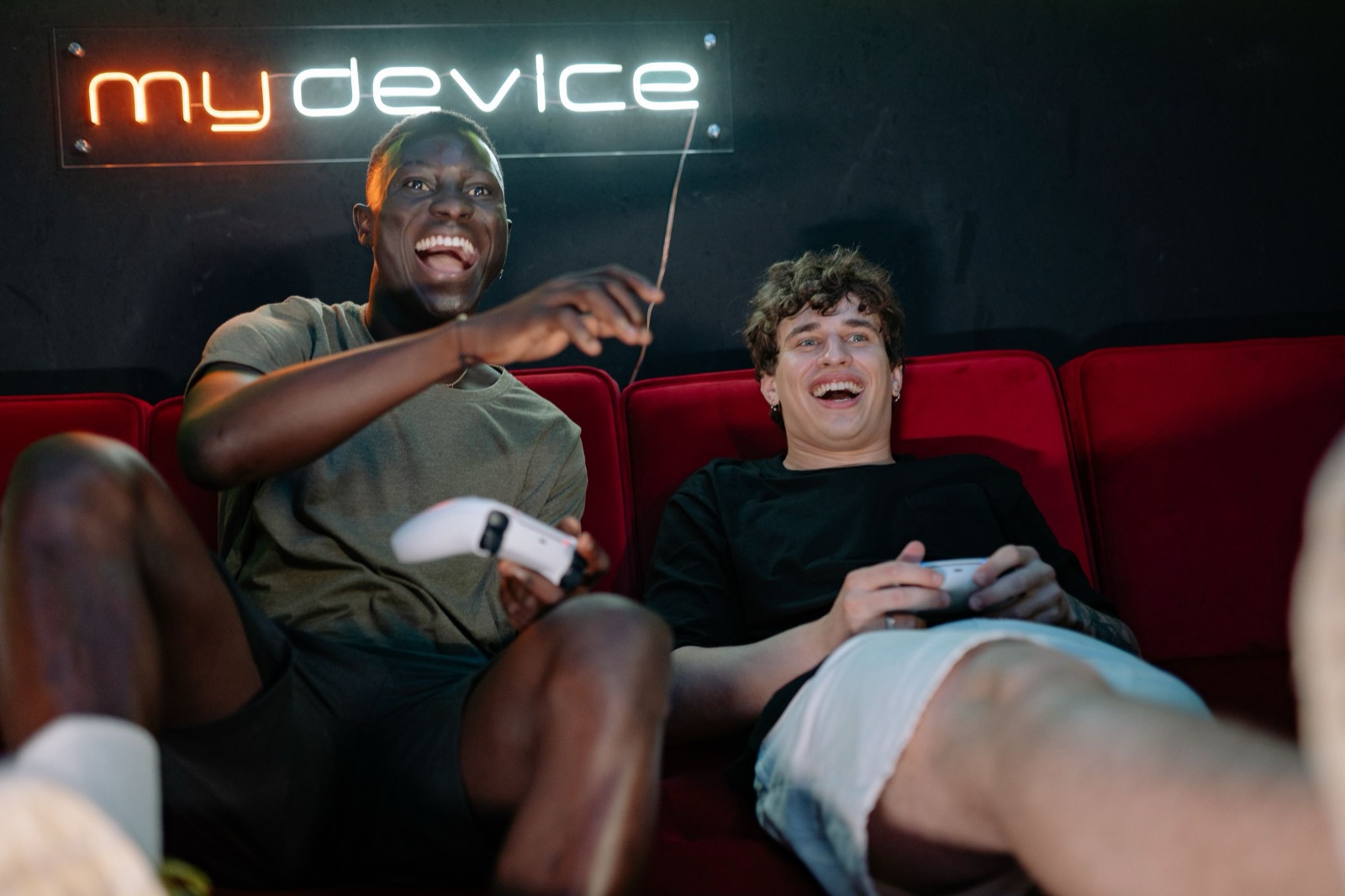 Due amici ridono mentre giocano insieme ai videogiochi con luci neon sullo sfondo